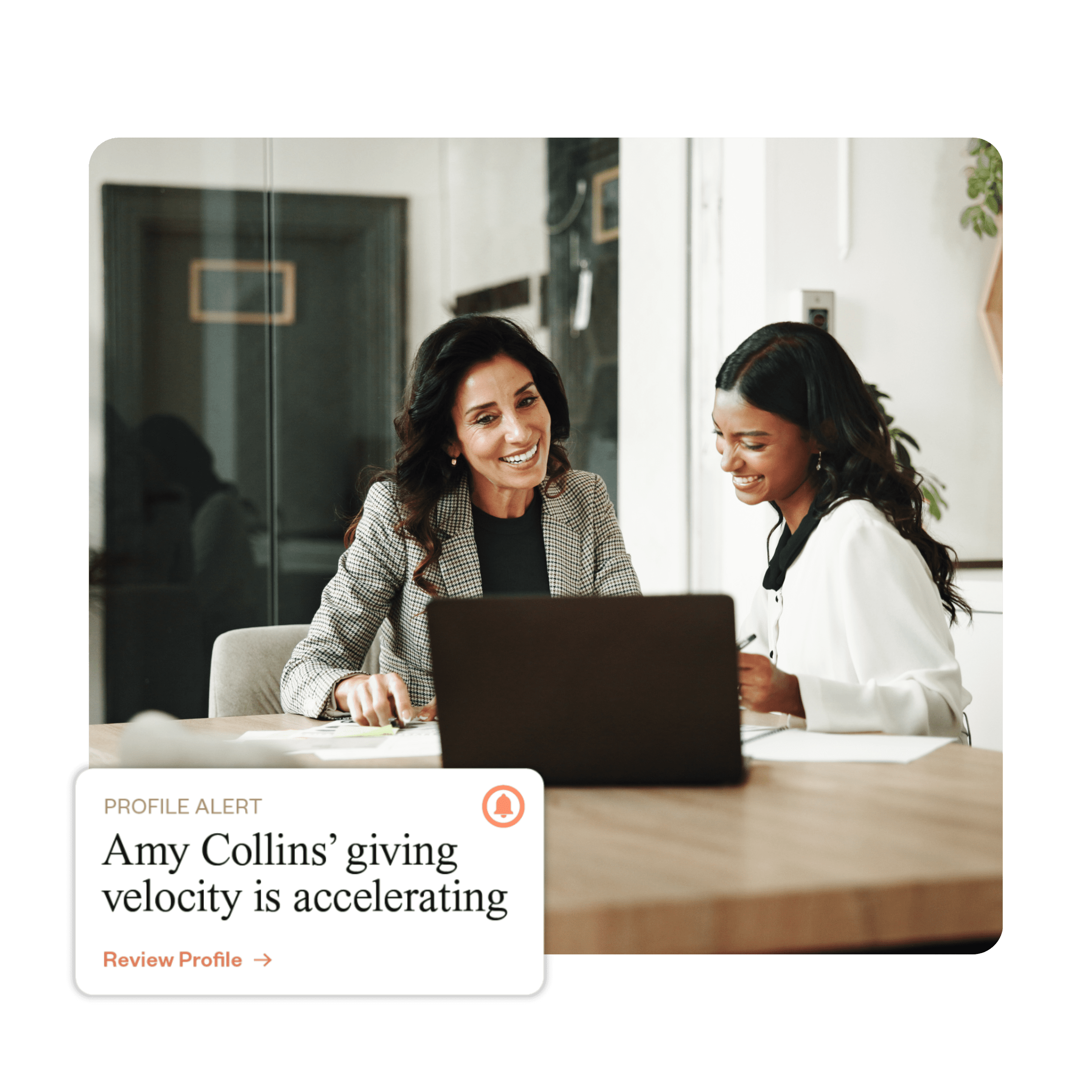 Two women smiling and collaborating at a desk with a laptop. A notification reads, "Amy Collins' giving velocity is accelerating." Bright and professional atmosphere.